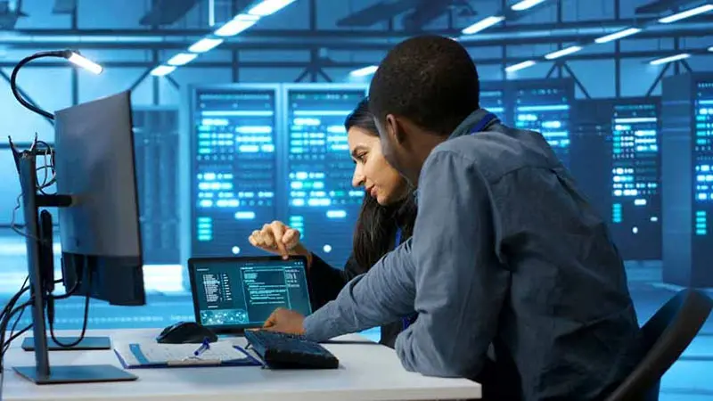 Computer engineers looking at a laptop discussing how to use ai based fraud detection in banking.