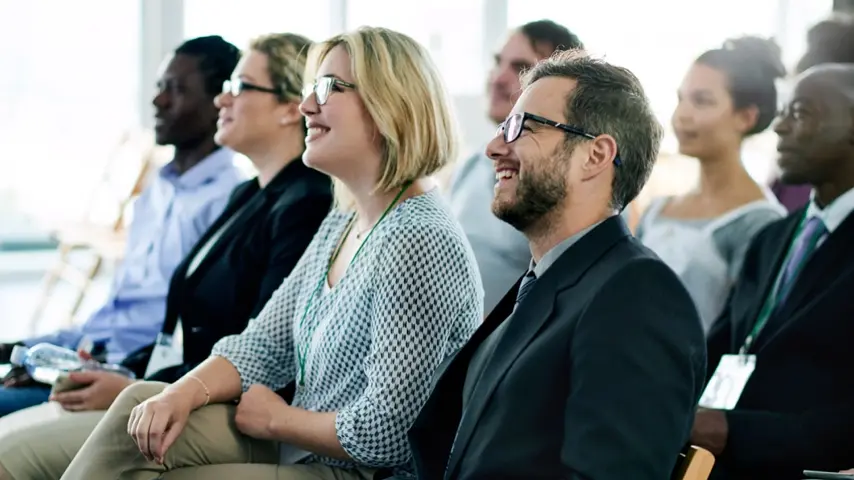 A group of people sitting down in a room facing the same direction  