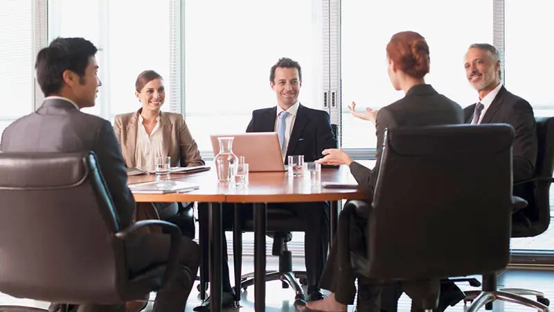 Office colleagues in a conference room at a table discussing digital payment and exchange agents for their business.