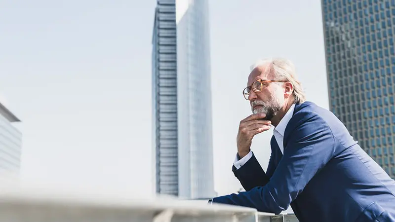 Man wearing a suit and glasses gazing at a skyscraper as he thinks about debt capital markets and settlement agents