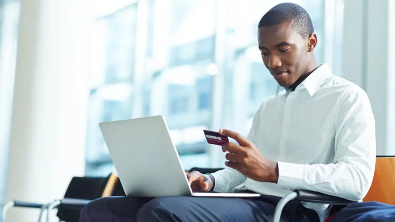 A man in a white shirt is sitting and using a laptop while holding a prepaid card