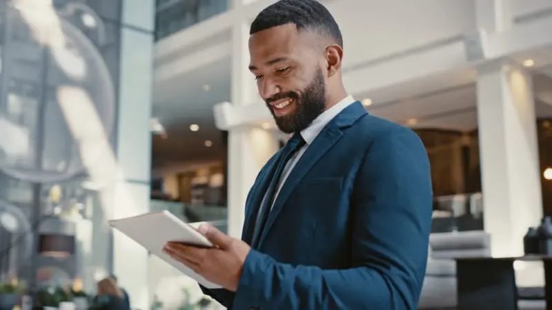A businessman in a blue suit smiles while using a tablet to conduct business
