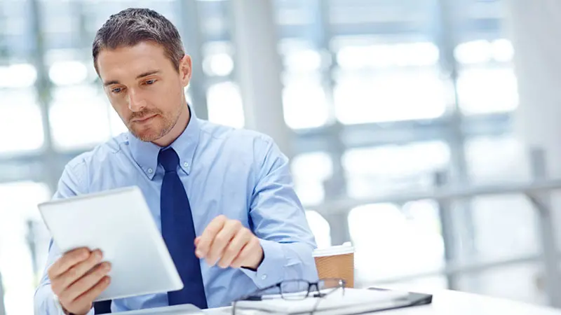 Professional man wearing a tie looking at a tablet device and reading about escrow