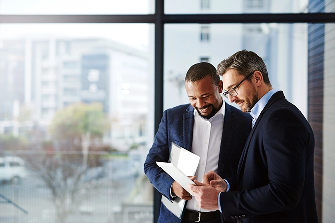 Two middle-aged men who are financial professionals, wearing suits and looking at a tablet device