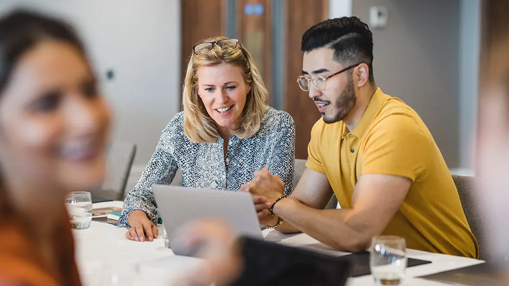 A person looking at a laptop while talking to another person