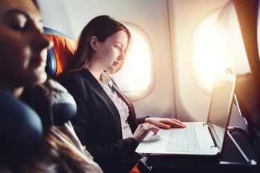 A person on an airplane viewing corporate travel solutions on their laptop