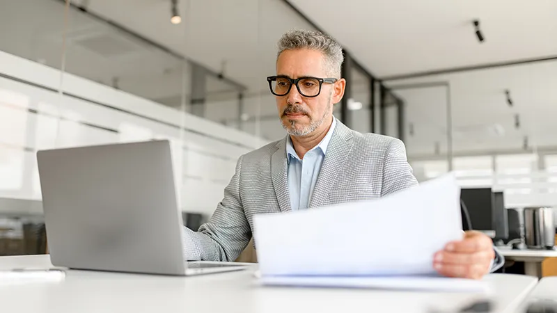 Person reviewing printed documents on how to transform credit payment while working on a laptop in a modern office setting.