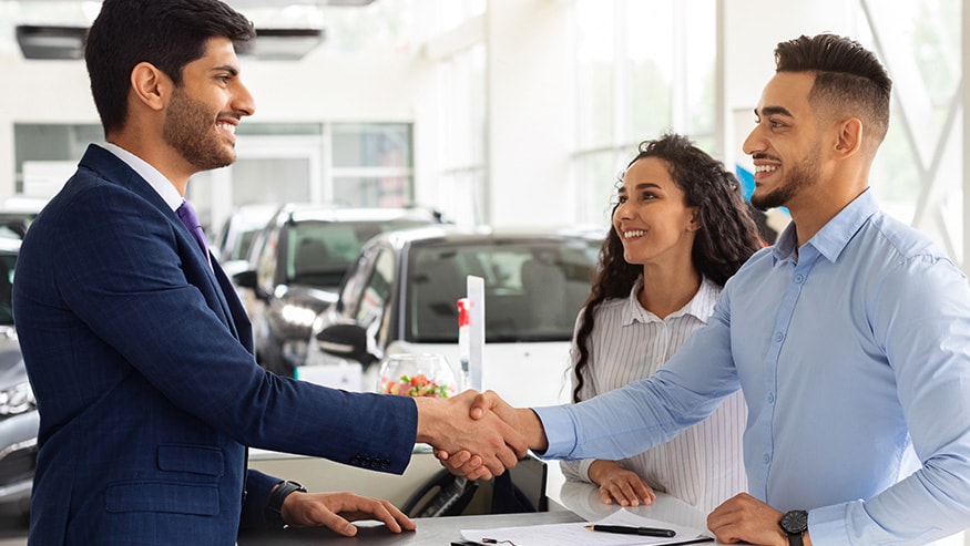 Young couple in a car dealership shaking hands with a salesman