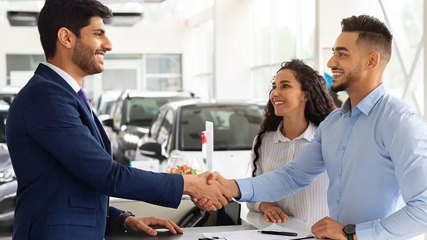 Young couple in a car dealership shaking hands with a salesman 