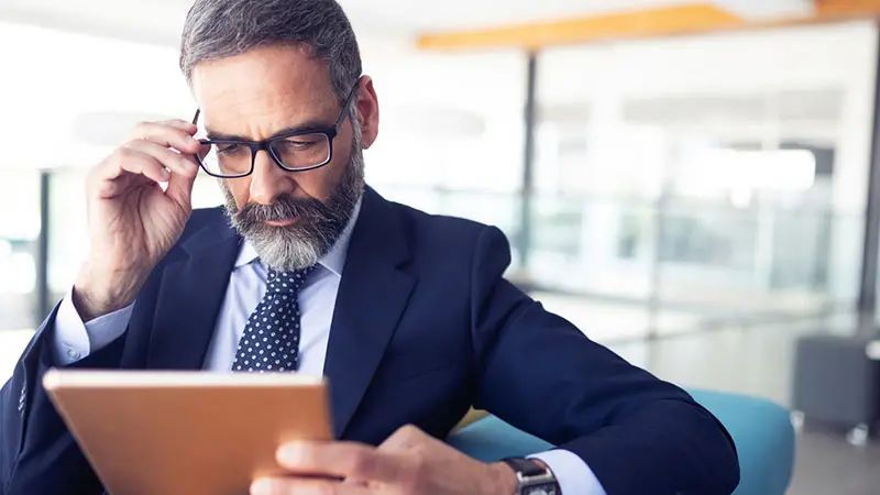 Bearded man using a tablet to read about investment fund onboarding
