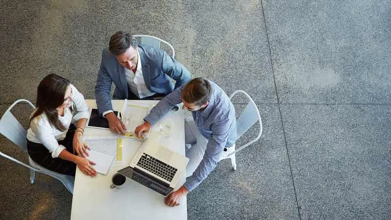 Three office workers sitting around table discussing the benefits of global corporate trustee service providers.