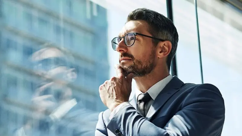 Man in suit and tie with hand under his chin as he gazes out the window