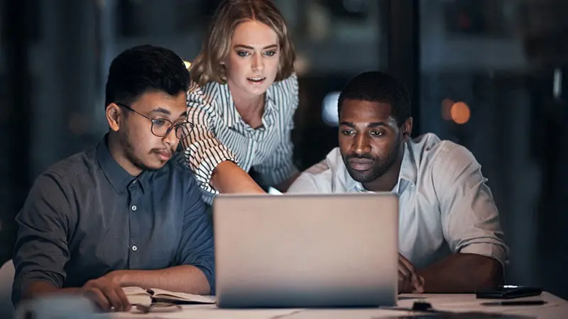 Three people looking at a computer evaluating payroll management prepaid cards