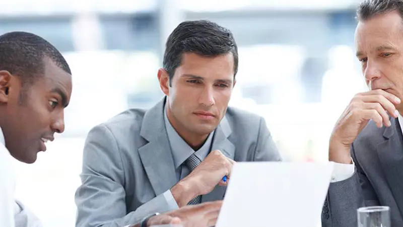 Three office men sitting around a computer discussing the role of authorized participants in the ETF process.