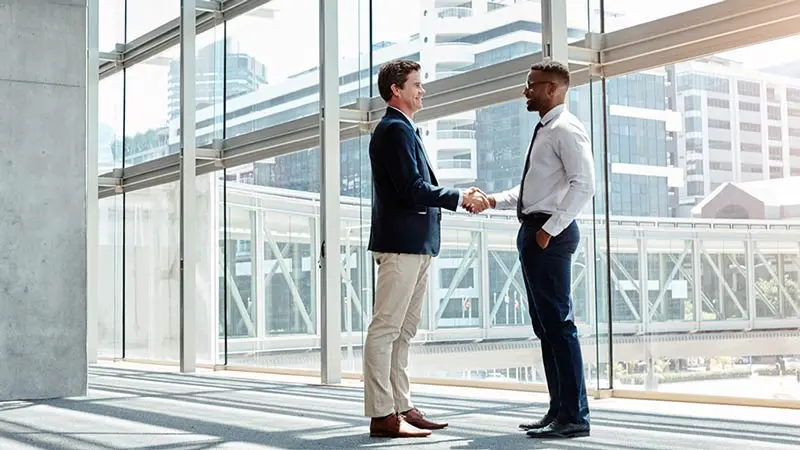 A private equity fund manager and private equity fund service provider shake hands in an office building.