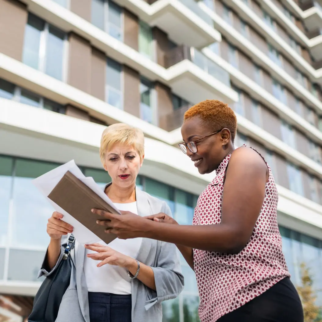 Two women standing next to each other looking at paperwork and checks and deciding how to handle them.
