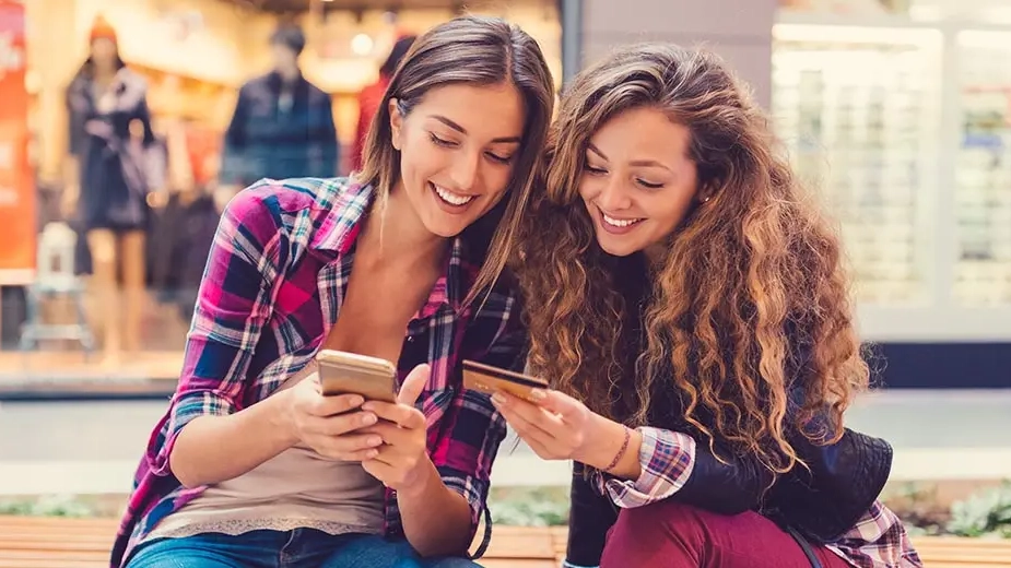 Two women in front of store looking at credit card and phone while making a government payment through an ebpp system.