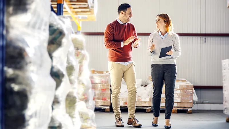 Business man and woman discussing logistics in warehouse.