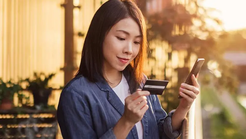 Woman holding phone and looking at her credit card