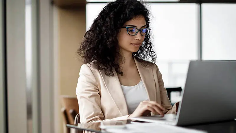Young professional woman sitting at a laptop and reading about questions to ask custody providers