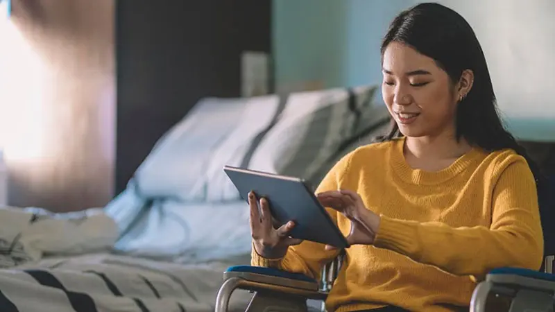 Woman in hospital room taps on a tablet that includes options for a better healthcare payment experience.