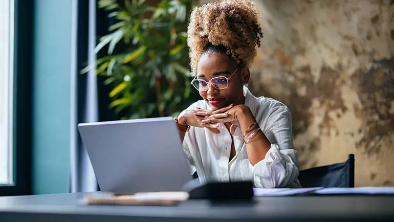 Woman sitting at a desk looking at a laptop.