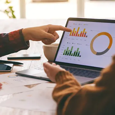 Two people looking and pointing at a chart on a laptop.