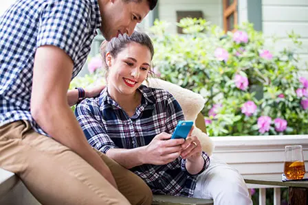 couple on porch looking at smartphone smiling