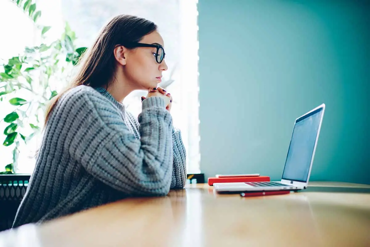 young woman wearing glasses staring intently at her laptop