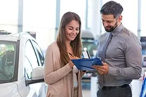 a woman writing on a clipboard at a car dealership