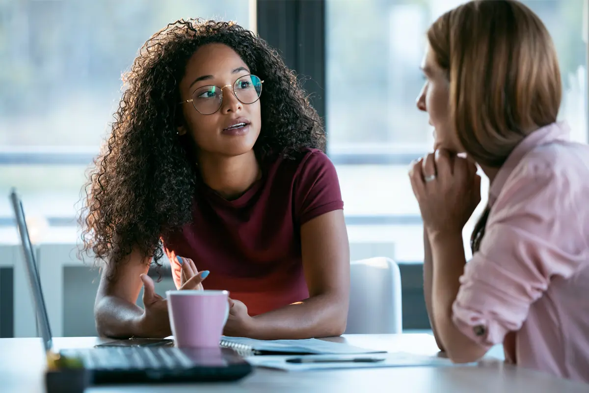 Two women talking with a pink coffee cup on the table in front of them