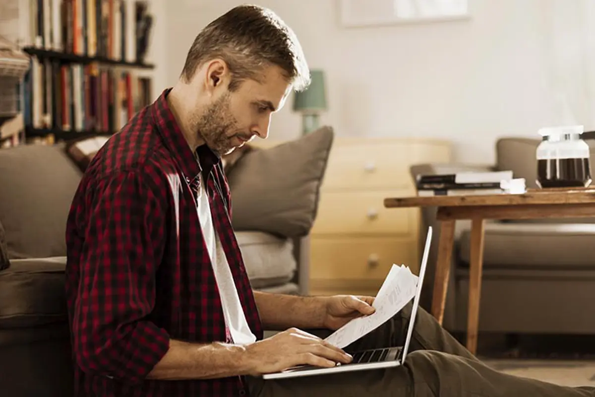 man in a red and black checkered shirt looking at a laptop
