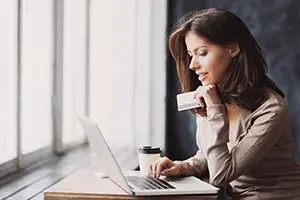a woman holding a credit card and working on her laptop
