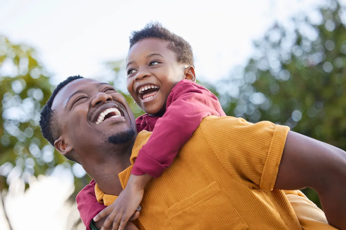 young boy enjoying a piggyback ride with his father in a garden