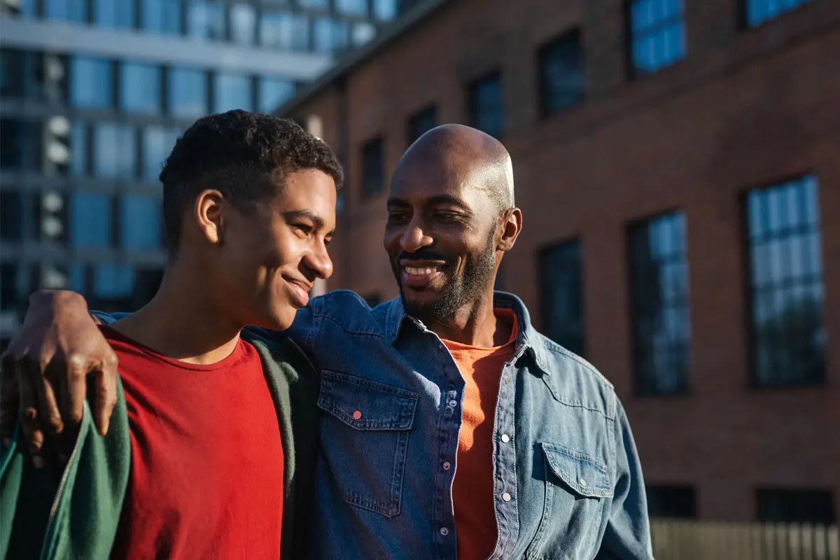 father with his arm around his young adult son walking on a street