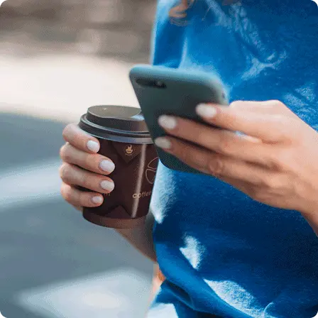 close up of a womans hands holding a coffee cup and a mobile phone