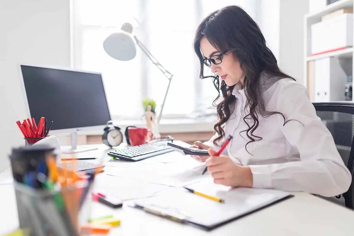 woman looking at calculator while sitting at her desk