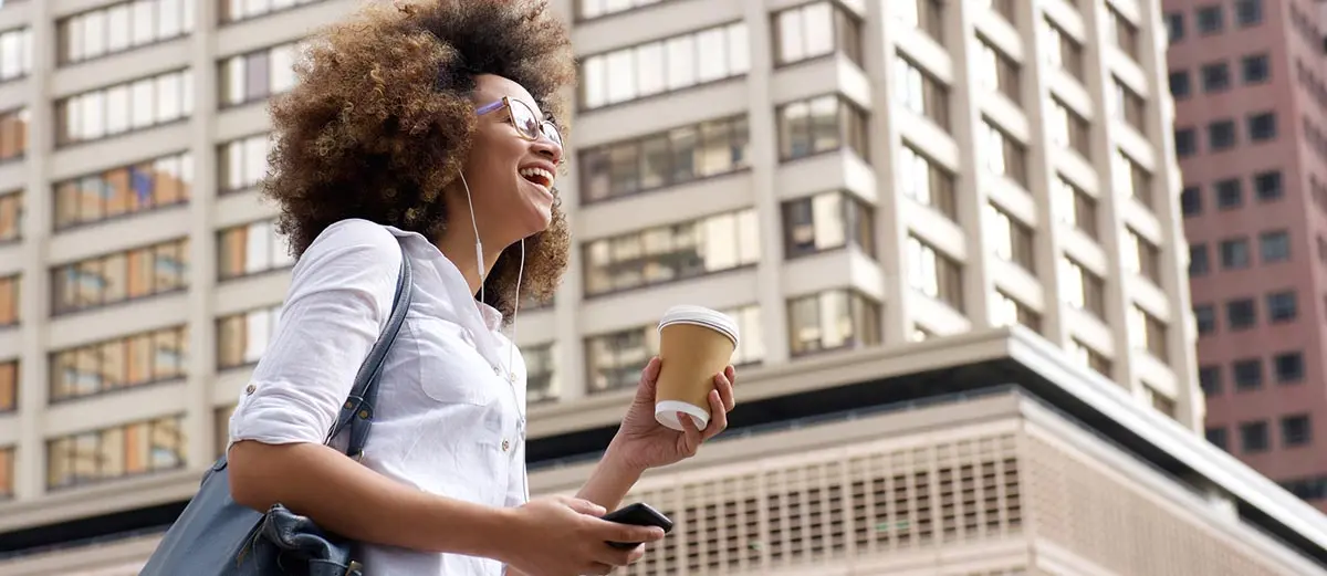 woman in a white shirt carrying a coffee cup in a downtown area