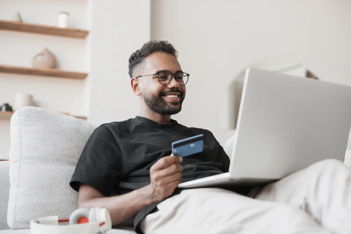 maon a white sofa holding a laptop and a credit card