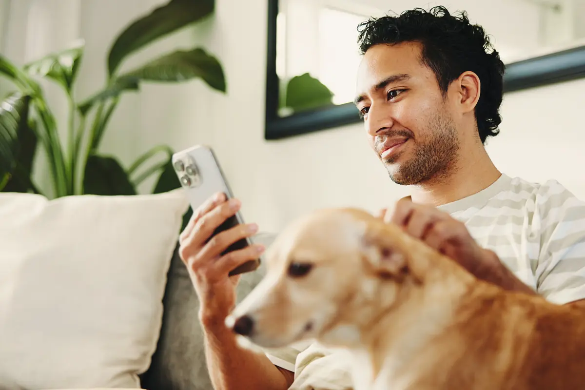 man petting his dog on the couch while looking at his phone