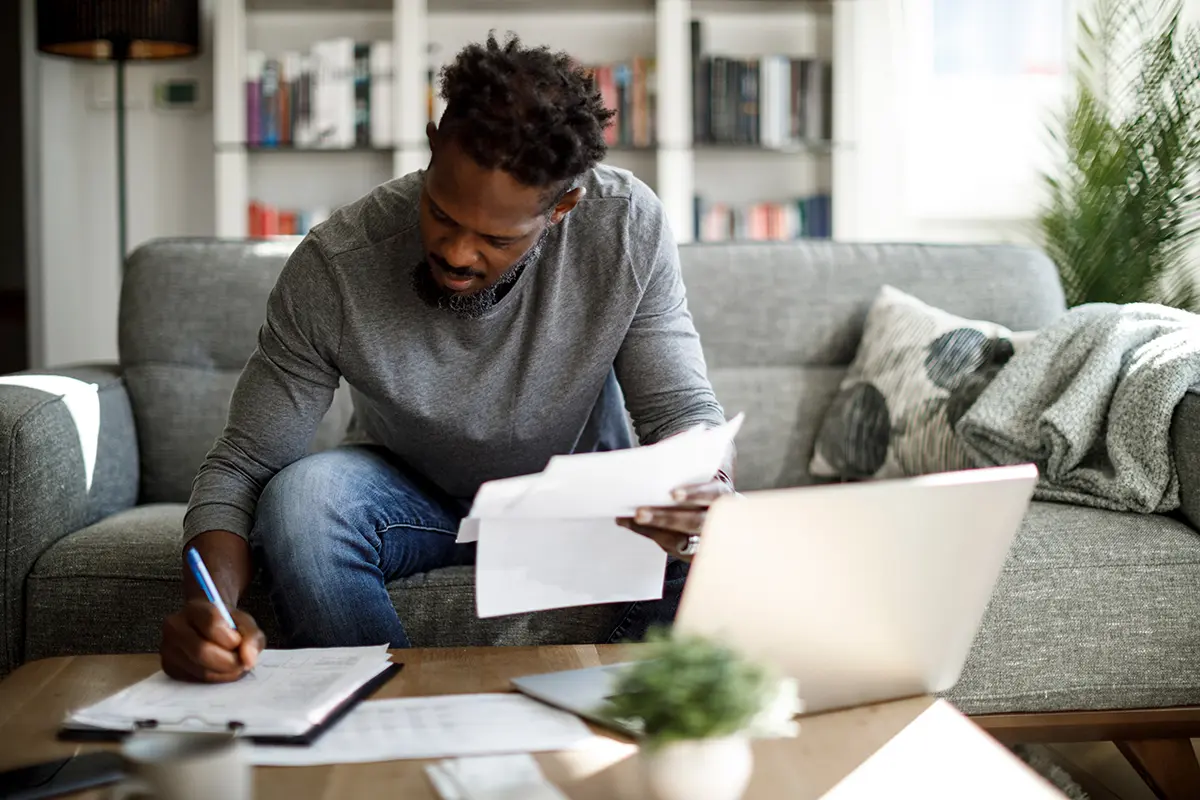 man in a grey shirt reading paperwork on a grey couch