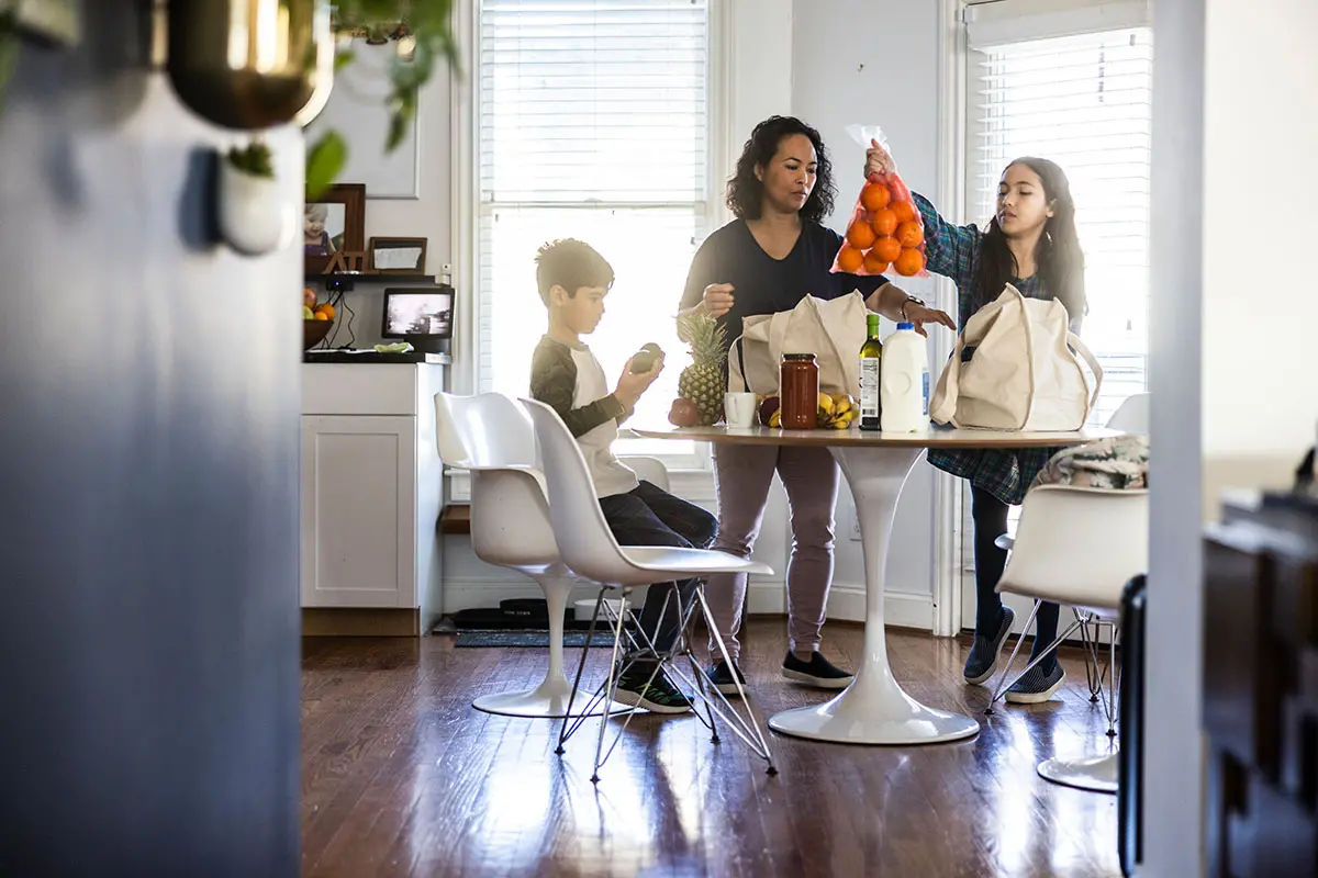 A mother with two children unpacking groceries at their kitchen table