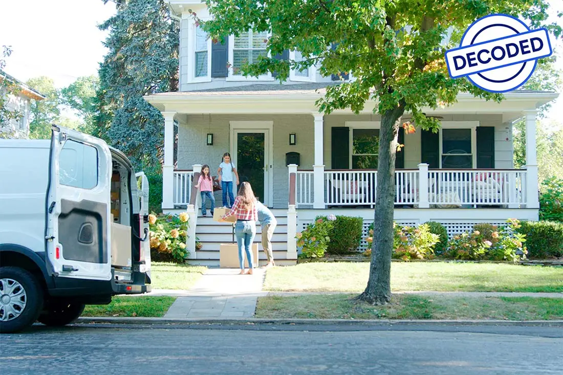 A woman and a man each carrying a box up the steps of a house while two children watch.