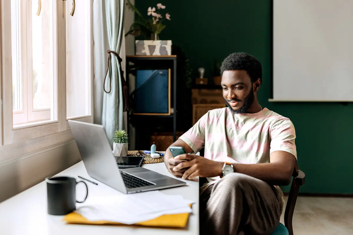 young man sitting at researching investment options on phone and laptop