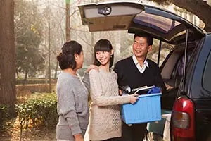 a man and a woman helping a young adult unpacking boxes from a vehicle