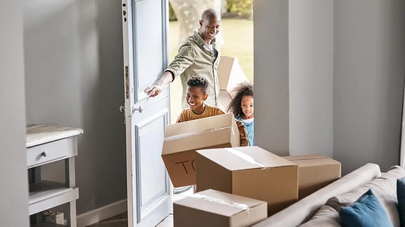 a father and his children walking into a home, carrying moving boxes