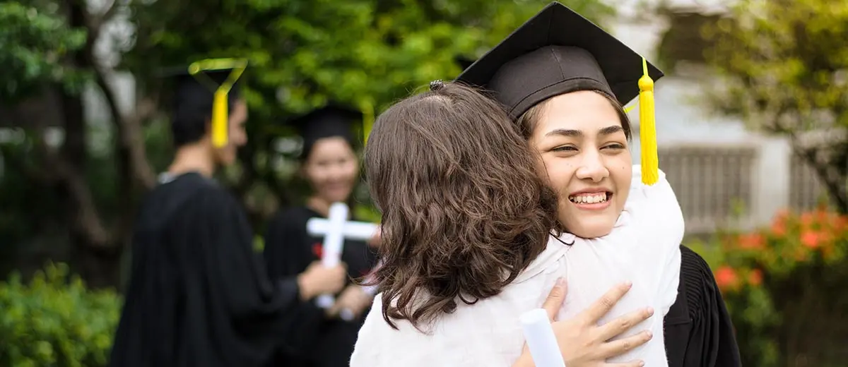 A woman in a graduation cap hugging a woman in a pink shirt 