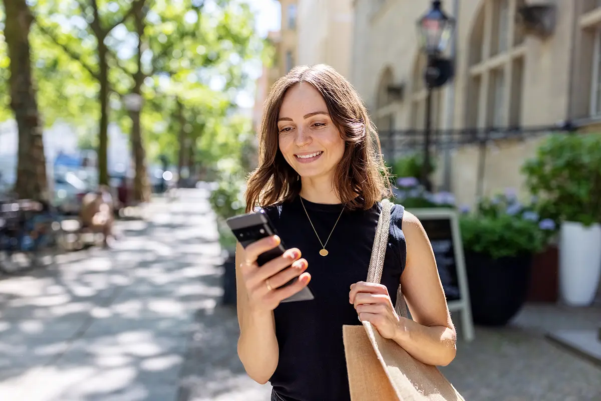 woman in a black shirt looking at her phone while walking on the street