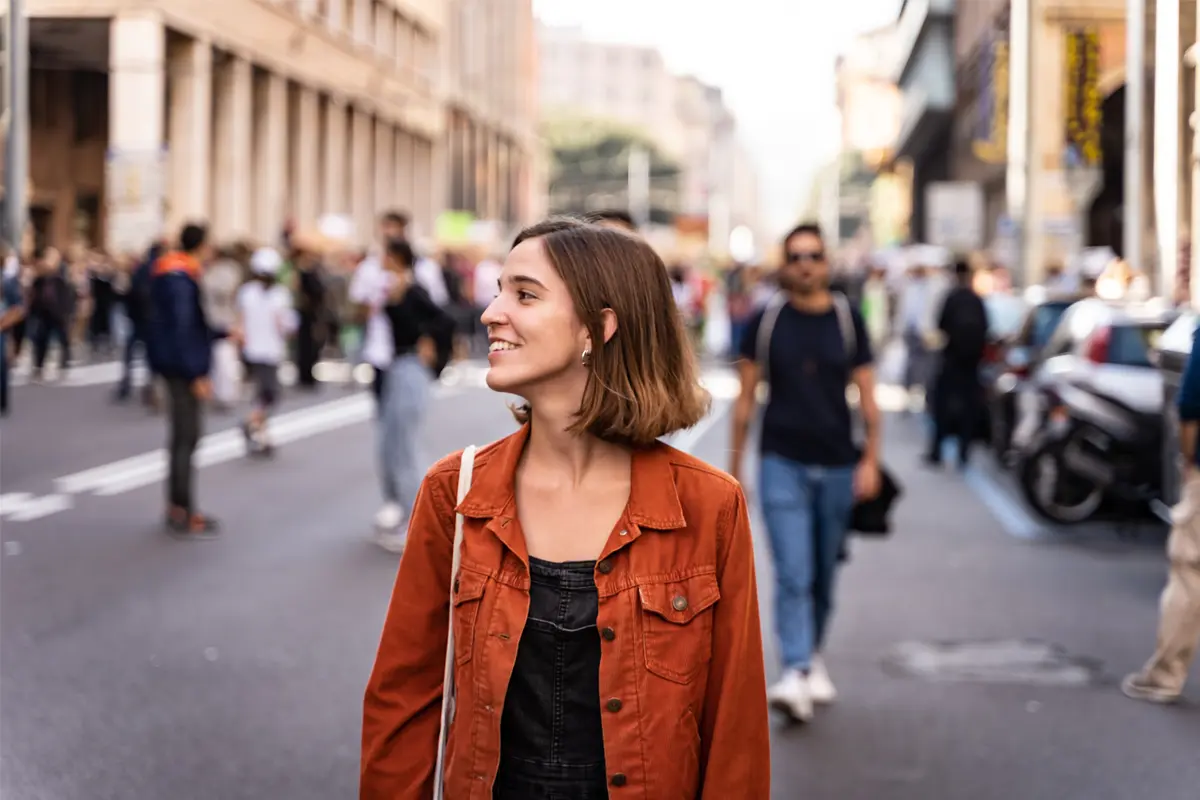 a woman in an orange jacket walking on a street and looking to the side