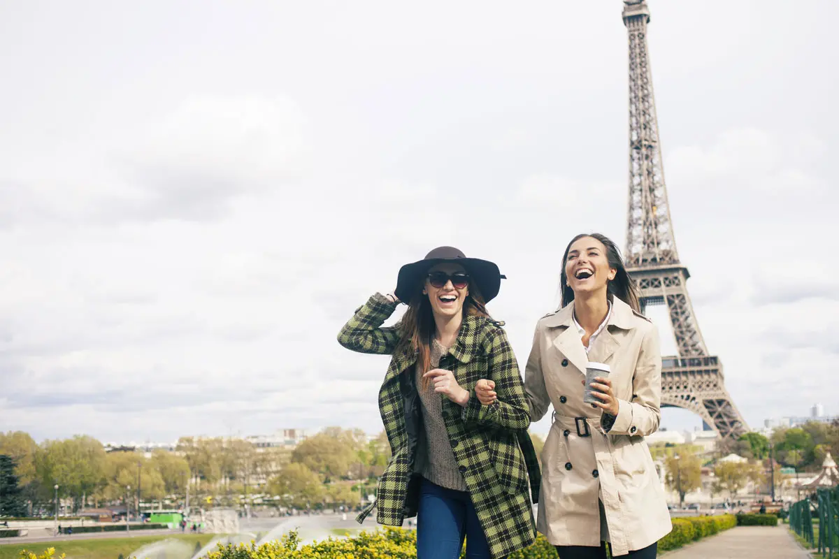 Two women laughing and walking in front of the Eiffel Tower